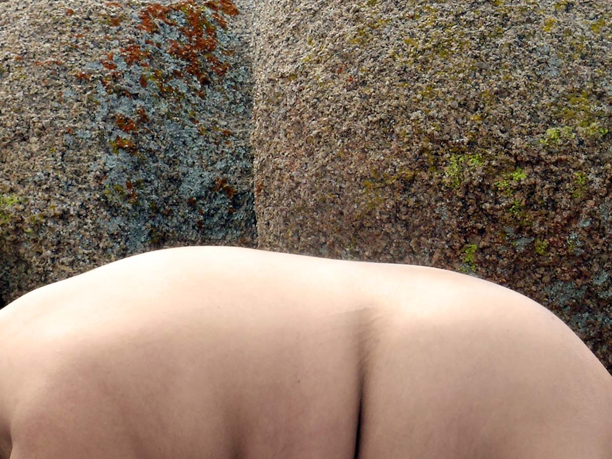 A boulder with lichen and a nude body in front of it, with a crease at the waist echoing in the fold of the boulder.