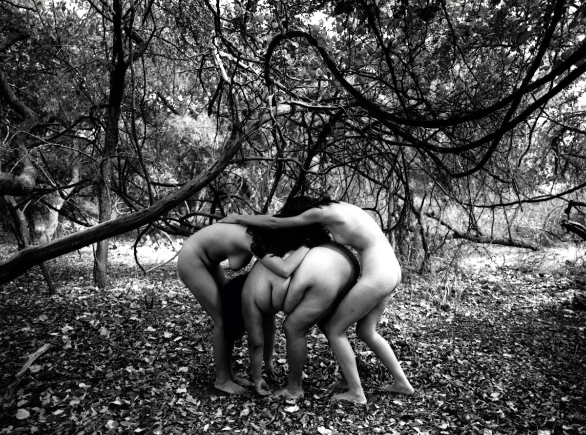 Black and white photograph by Laura Aguilar of three women posing amid curved, intertwined tree branches