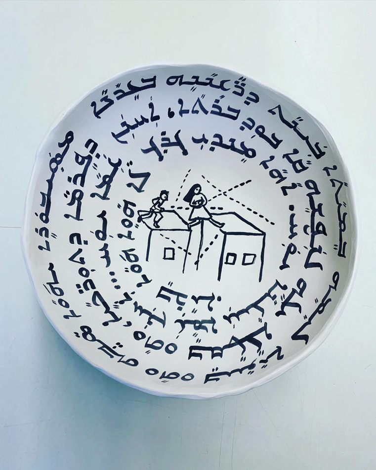 White clay prayer bowl with black text and an image in the center made by Esther Elia from the workshop she hosted in Arizona.