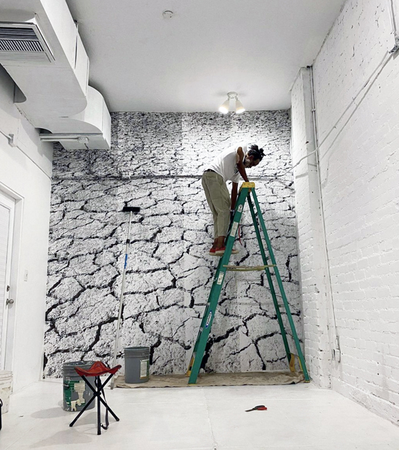 Chip Thomas stands on a ladder and installs artwork at Snakebite Creation Space