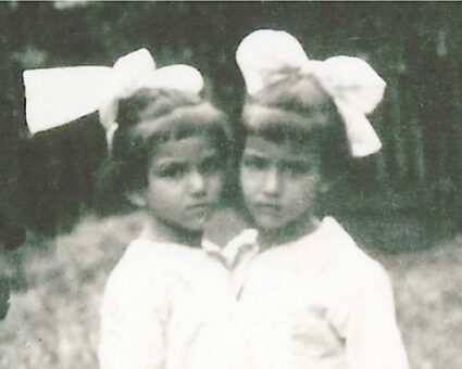Black and white photograph of twin girls, conjoined at the chest, wearing oversized large bows in their hair.