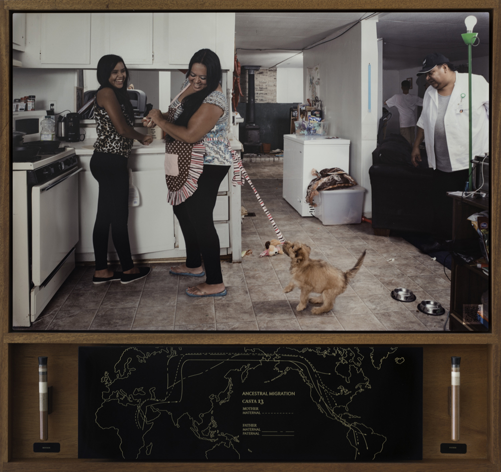 Delilah Montoya, Casta 13 from Contemporary Casta Portraiture: Nuestra Calidad, 2018, photograph and mixed media. Photograph shows two women laughing in a kitchen, with a puppy pulling at the apron tied around one woman’s waist. Two men are in the peripheral view of the scene. Lower half shows ancestral migration routes generated from parental DNA test results.