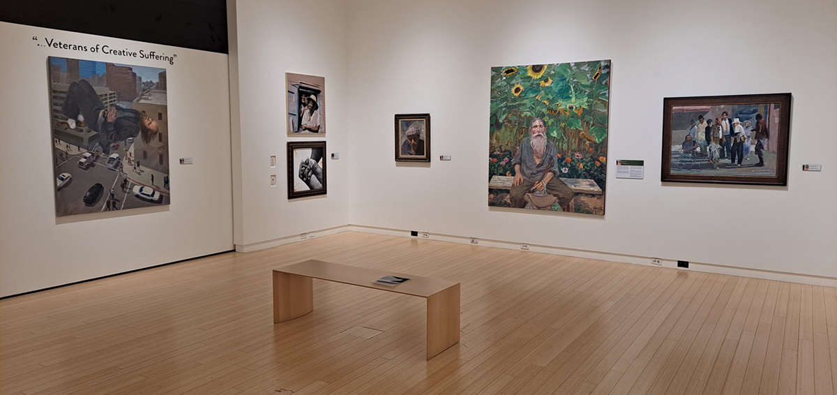 Installation view of an exhibition at the Mesa Arts Center, with wall text that reads "Veterans of Creative Suffering" and various paintings hung on the walls.