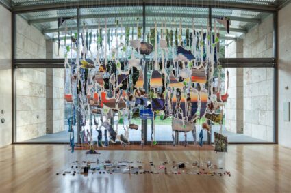 A work by Sarah Sze, hanging from the ceiling are photographs of nature cut into and grounded by objects used in its creation.