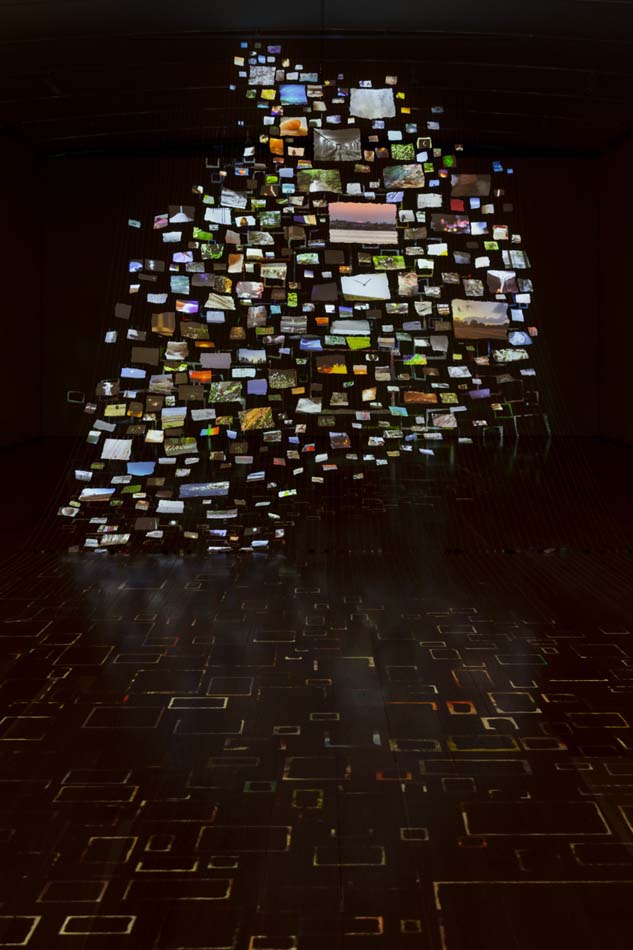 In a darkened room a cloud of individual projected images on paper, string aluminum, and mixed media by Sarah Sze.