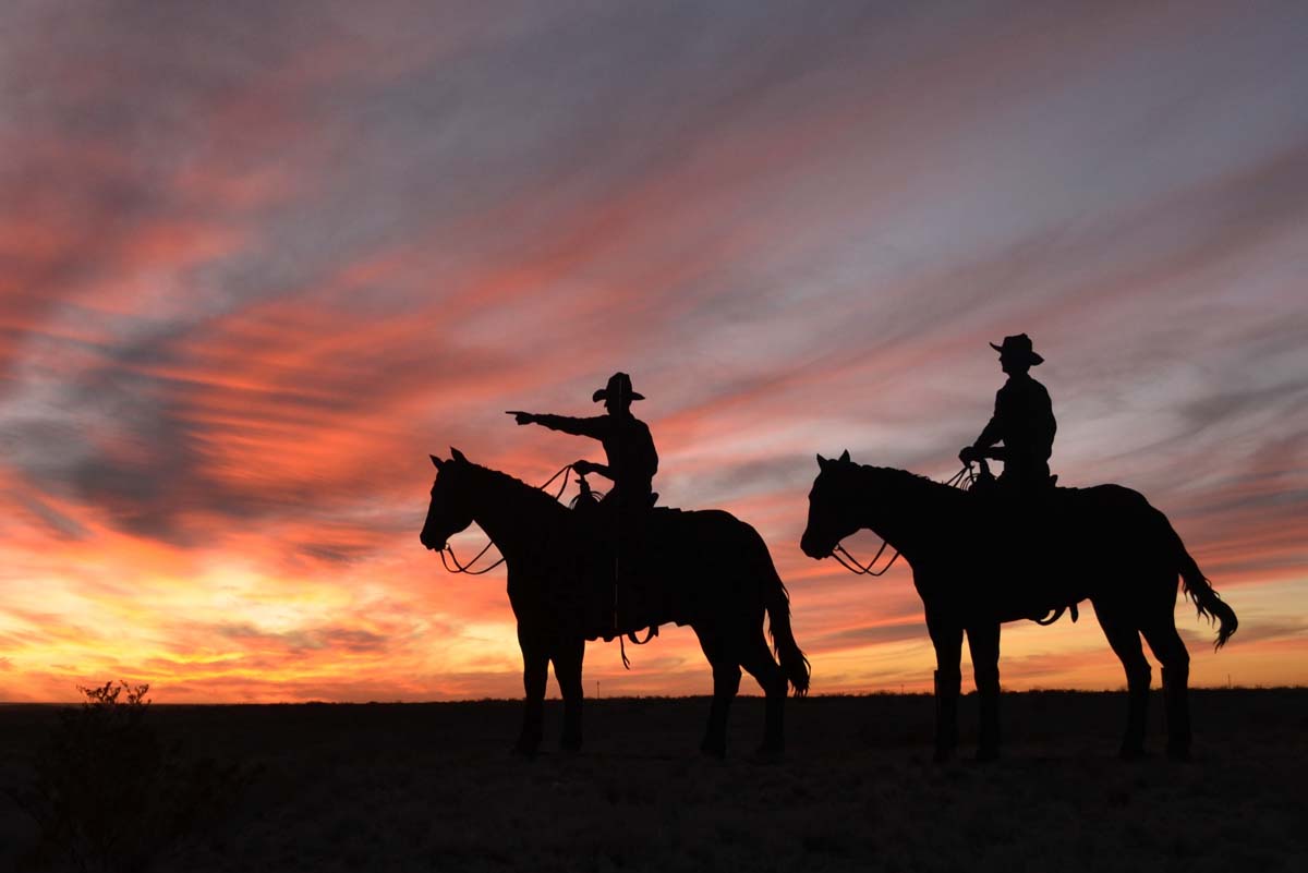 Silhouettes of two cowboys on horseback with a sunset behind them.
