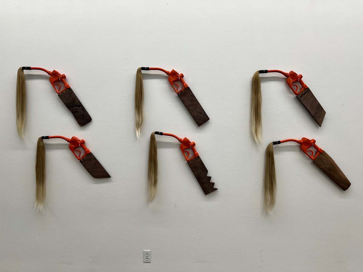 Six gas pump sculptures of orange ceramic, wooden paddles, and blonde hair coming out of the spouts.