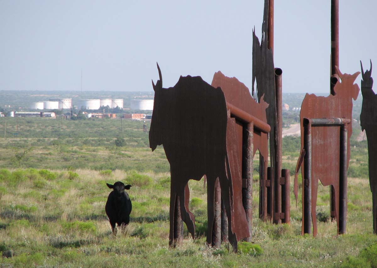 A cow standing next to a group of monumentally sized steel sculptures.