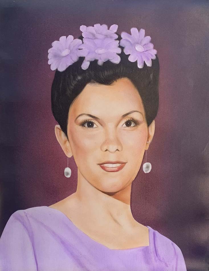 Portrait of a young woman wearing violet, earrings, and with violet flowers in her dark hair in an up-do.