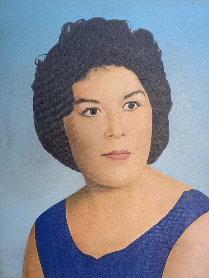 Portrait of a young Mexican woman with short black hair wearing a blue top with a light blue background.