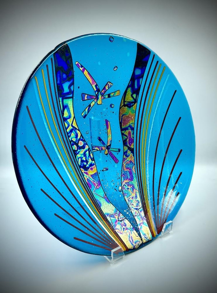 Round fused glass artwork with blue dragonfly motif.