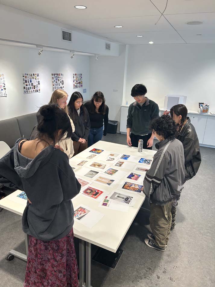 A group of young people standing around a table with art reproductions arranged across it.