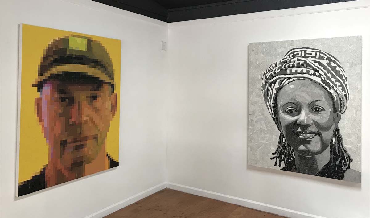 Installation view with two large-scale paintings, on the left a man wearing a hat with an overall yellow hue throughout, on the right, a woman wearing a head scarf, in black and white.