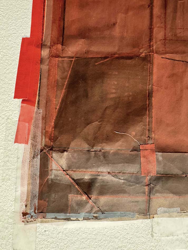 A detail view of a collage made of red and brown paper with tape and threads.