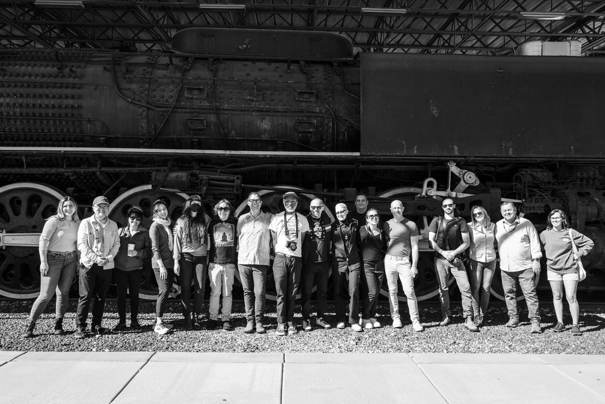 Participants in the train journey that inspired railroad-themed art exhibition The Other Side of the Tracks pose in front of a steam engine.