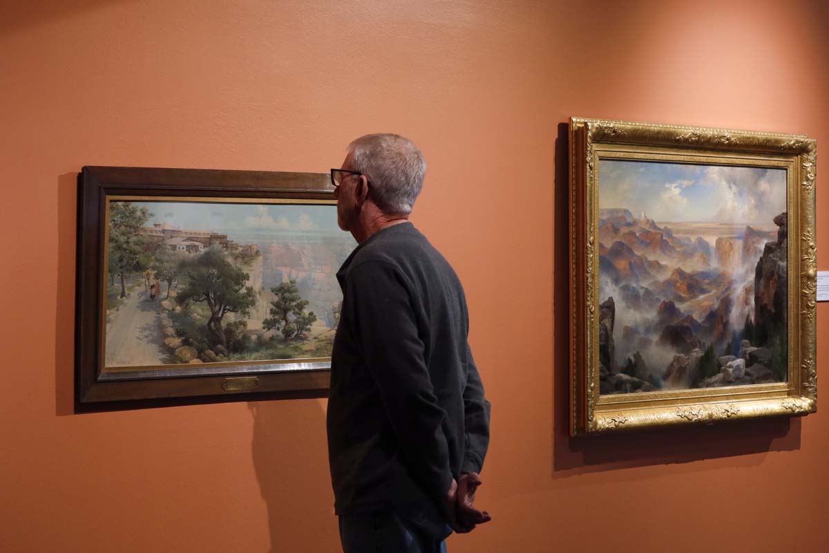 Man viewing two Southwestern landscape paintings hung on an orange wall.