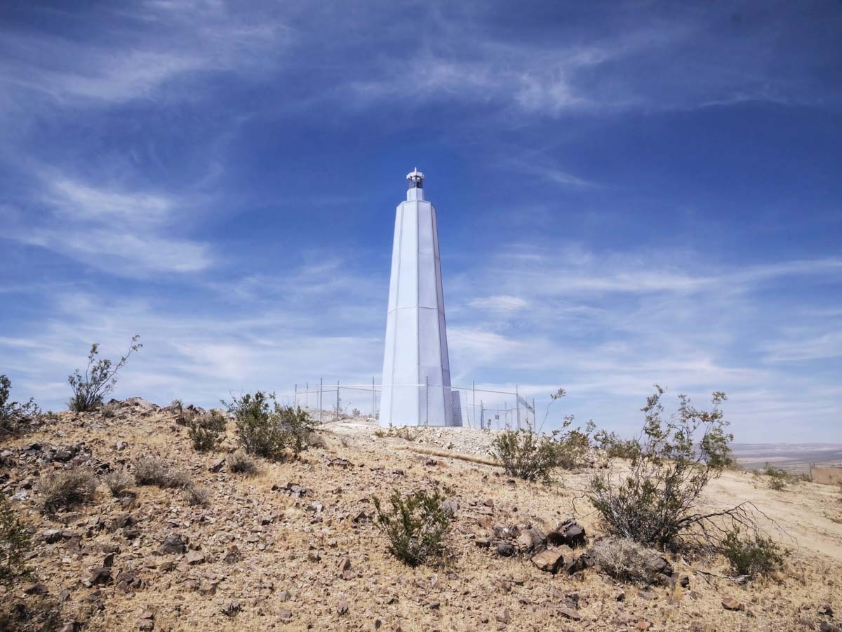 A white lighthouse on a hill with scrubby creosote bushes.