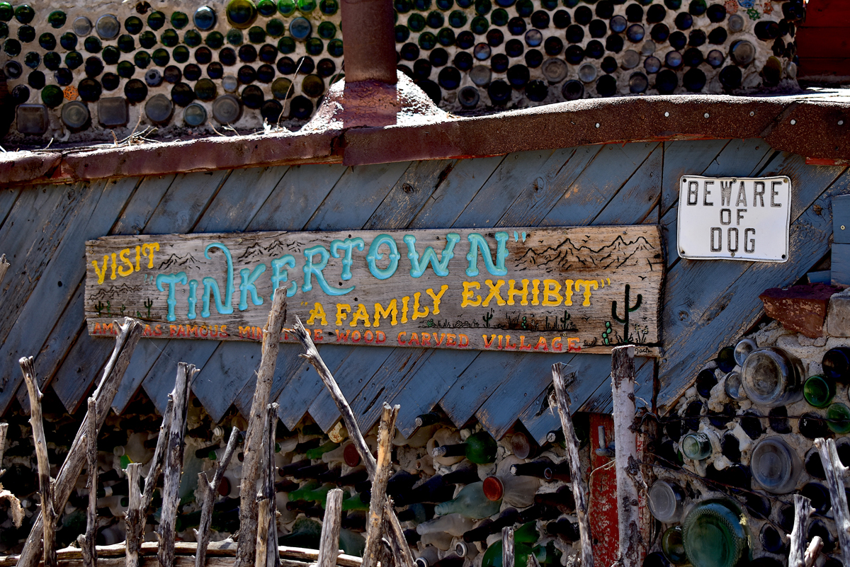 A yellow and turquoise sign carved from wood reads "Visit Tinkertown, a Family Exhibit." A cheeky sign next to it reads "Beware of Dog."