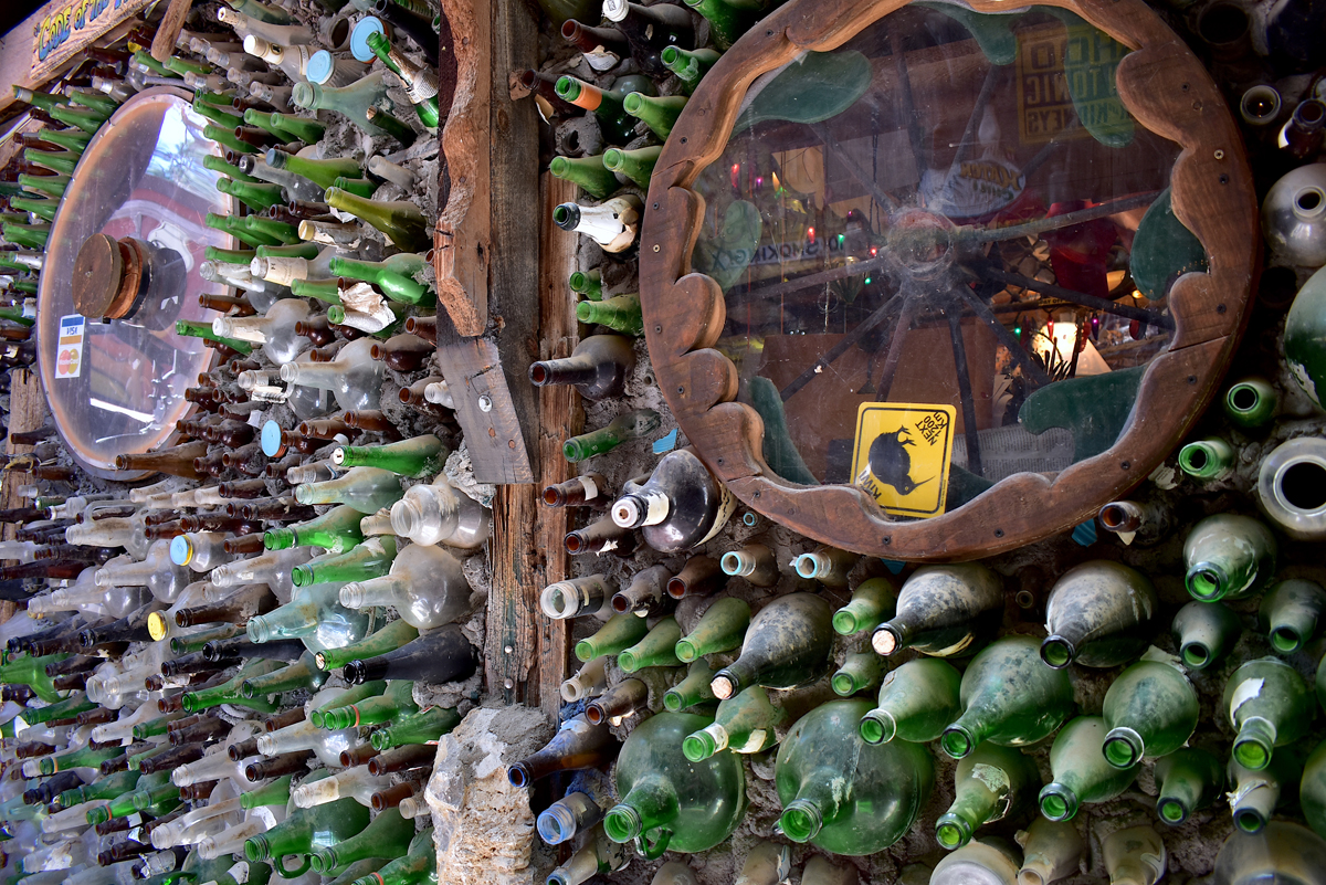 A wall made from hundreds of stacked bottles with inset wagon wheel windows at the Tinkertown Museum, a famous New Mexico roadside attraction.