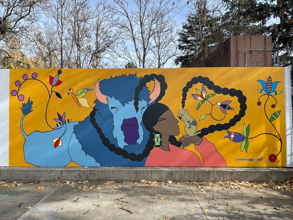 Mural by Danielle SeeWalker featuring a Native woman, a blue buffalo, and animal life including a butterfly and a groundhog. 