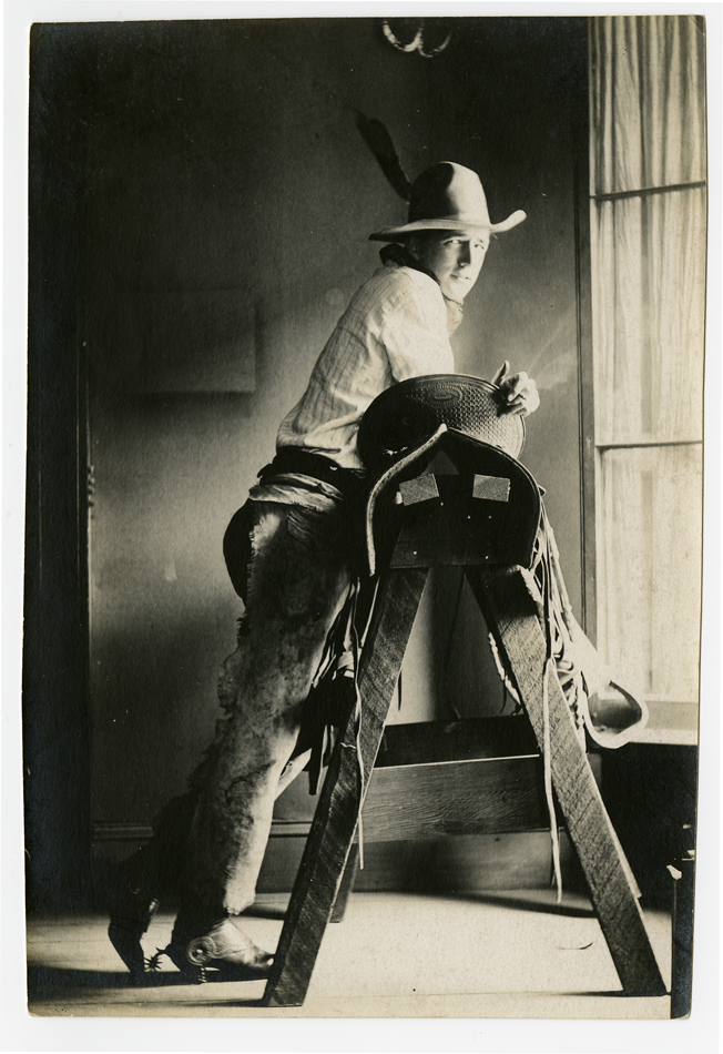 Portrait of the American modernist Maynard Dixon, dressed as a cowboy and leaning against a sawhorse with a beguiling expression.