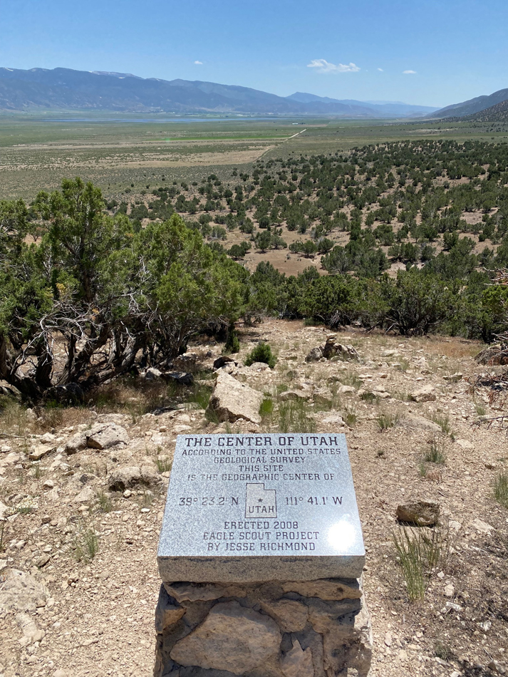 Granite placard that reads "The Center of Utah" overlooking a Southwestern vista.