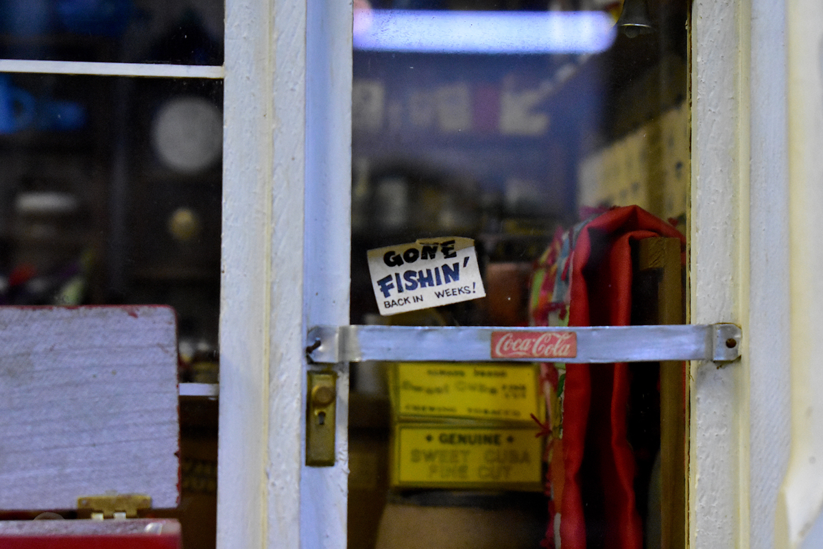 Detail of a miniature store's front door, with a sign that says "Gone Fishin', back in weeks!" 