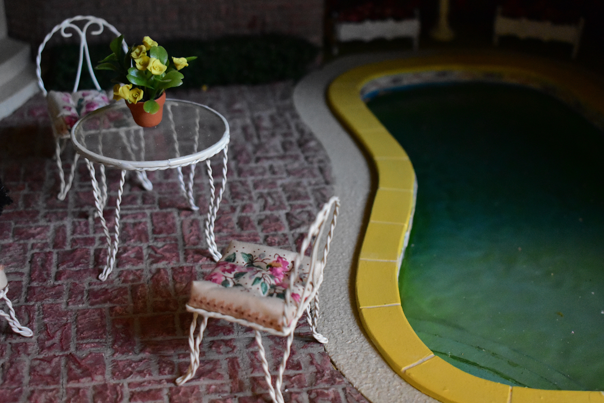 Detail of the exterior of a miniature house, showing a pool and patio furniture.