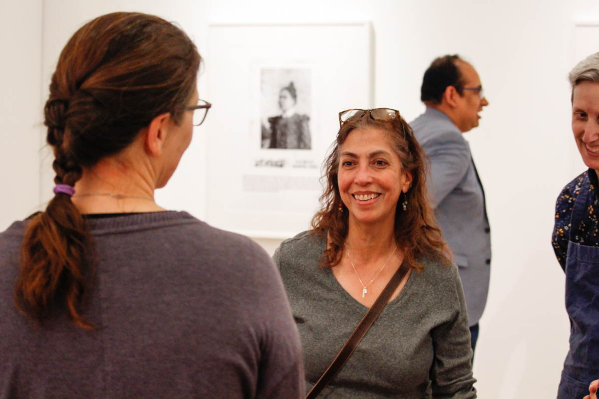 Artist Annie Lopez at the opening of her new solo exhibition at the University of Arizona. Behind her is a framed photograph.