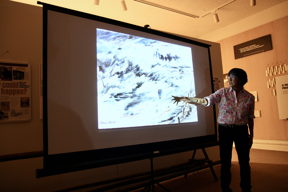 The granddaughter of Chiura Obata, who started an art school at a Japanese American concentration, gestures at a projected image of one of his artworks.