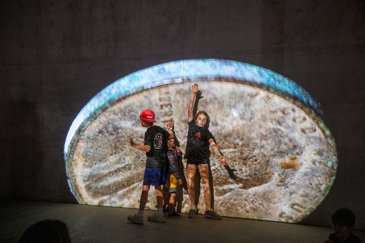 Two children in front of a massive projected image of an old penny.