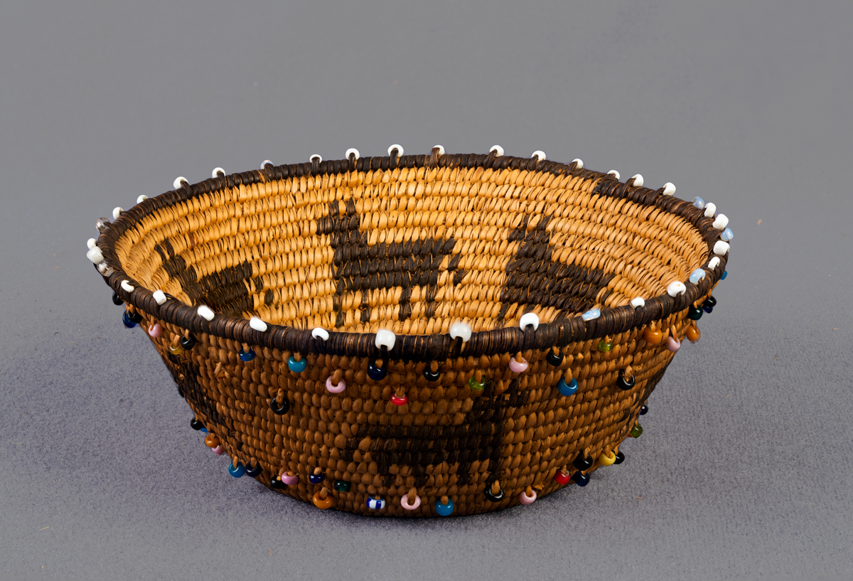 An Indigenous basket covered in colorful beads. This image is featured in Woven from the Center, a new book on Native basketry by Diane Dittemore.