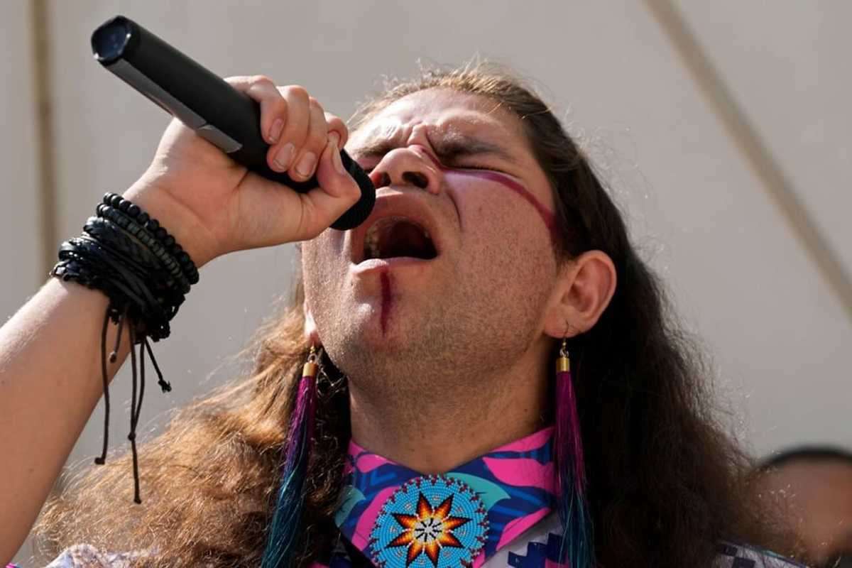 Musician Big Wind, one of many Indigenous artists exhibiting in conjunction with this year's Santa Fe Indian Market. He sings passionately into a microphone.