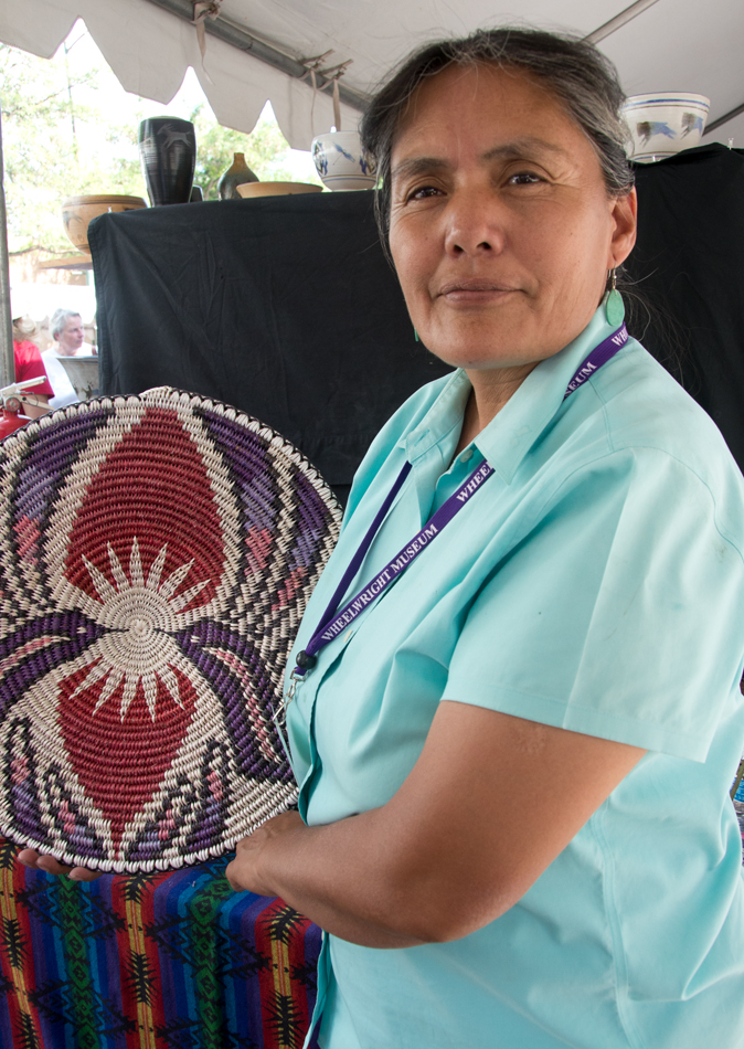 An Indigenous basket weaver holds one of her words, featuring a double hummingbird motif. This image is featured in Woven from the Center, a new book on Native basketry by Diane Dittemore.