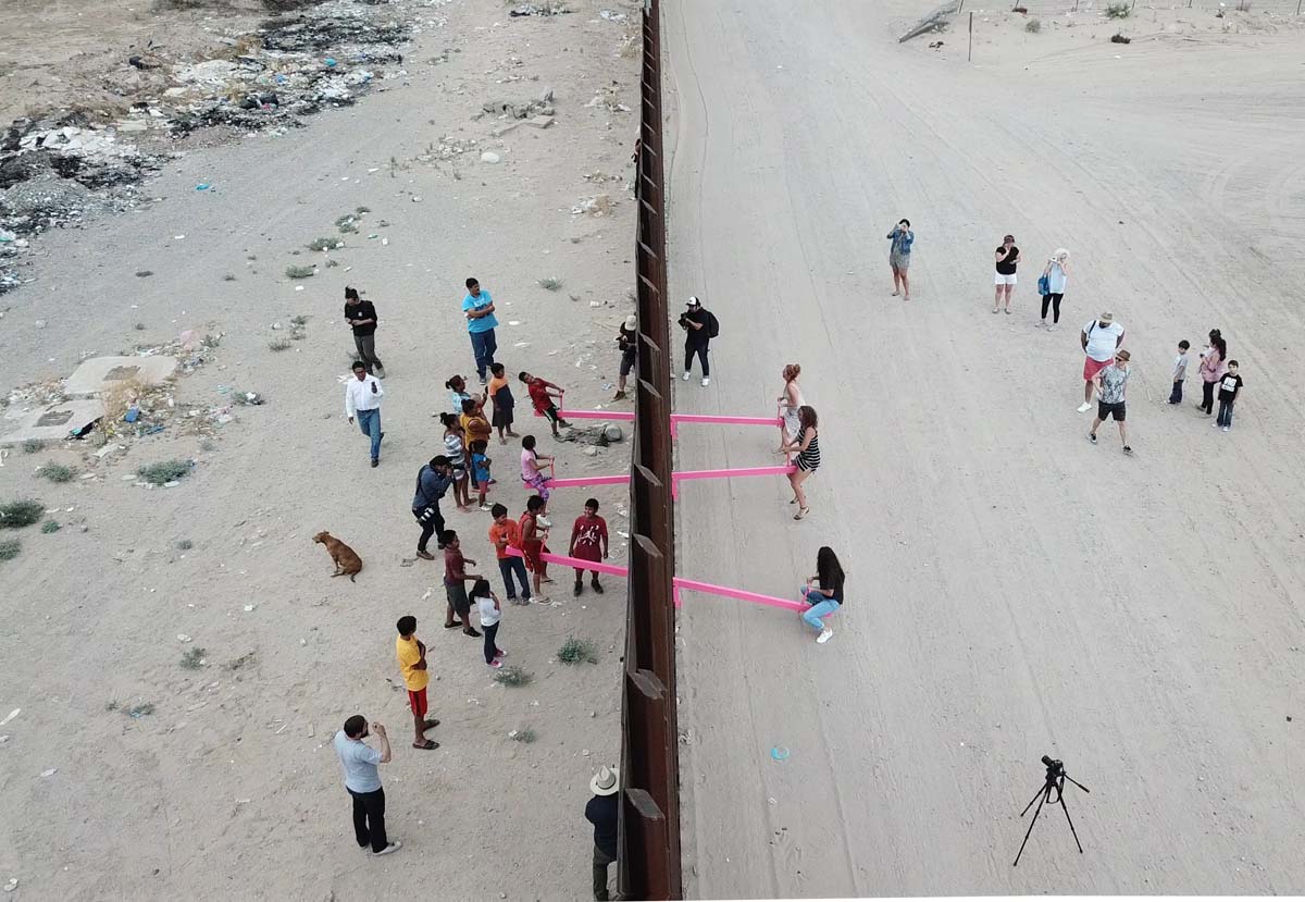 Pink teeter totters arranged through the US-Mexico border wall.