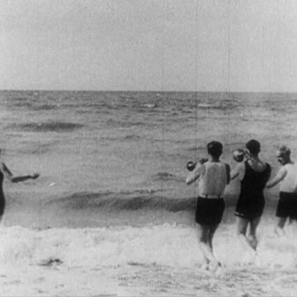 Still of a black and white film of people playing at the beach just before WWII.