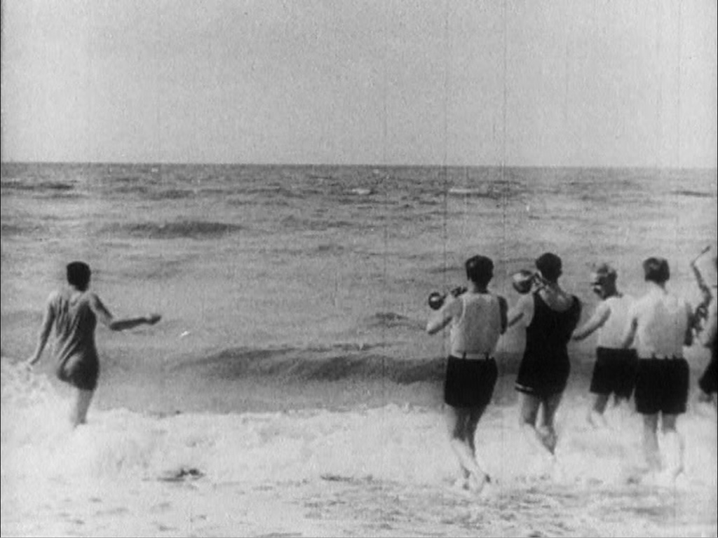 Still of a black and white film of people playing at the beach just before WWII.