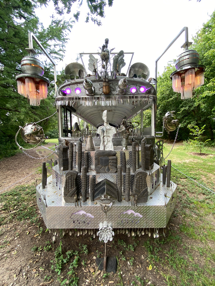 A chrome bus covered with biomorphic metallic sculptural elements made from found materials. Installation view of Guadalape Maravilla's interactive, kinetic bus sculpture Mariposa Relampago.