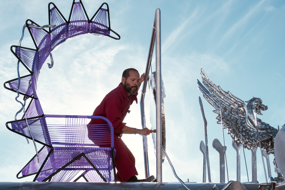 A man rises from a purple throne to play a gong. Guadalupe Maravilla Mariposa Relampago is a musical, winged bus with its own migration narrative.