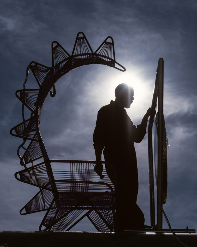 A man plays a gong, silhouetted in the sun. Guadalupe Maravilla Mariposa Relampago is a musical, winged bus with its own migration narrative.