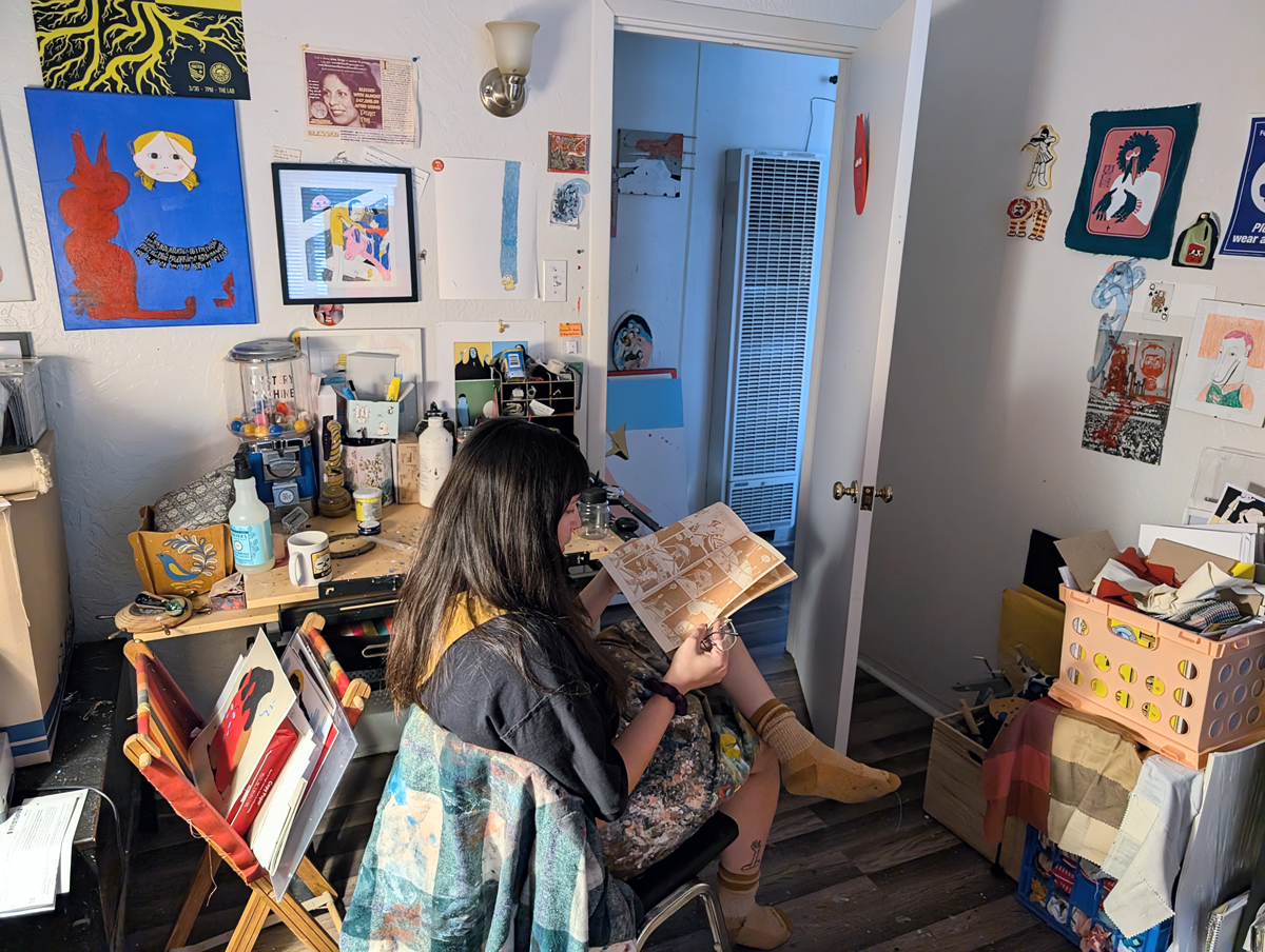 Beedallo pores over a Gumby comic, surrounded by artworks in their Albuquerque studio.