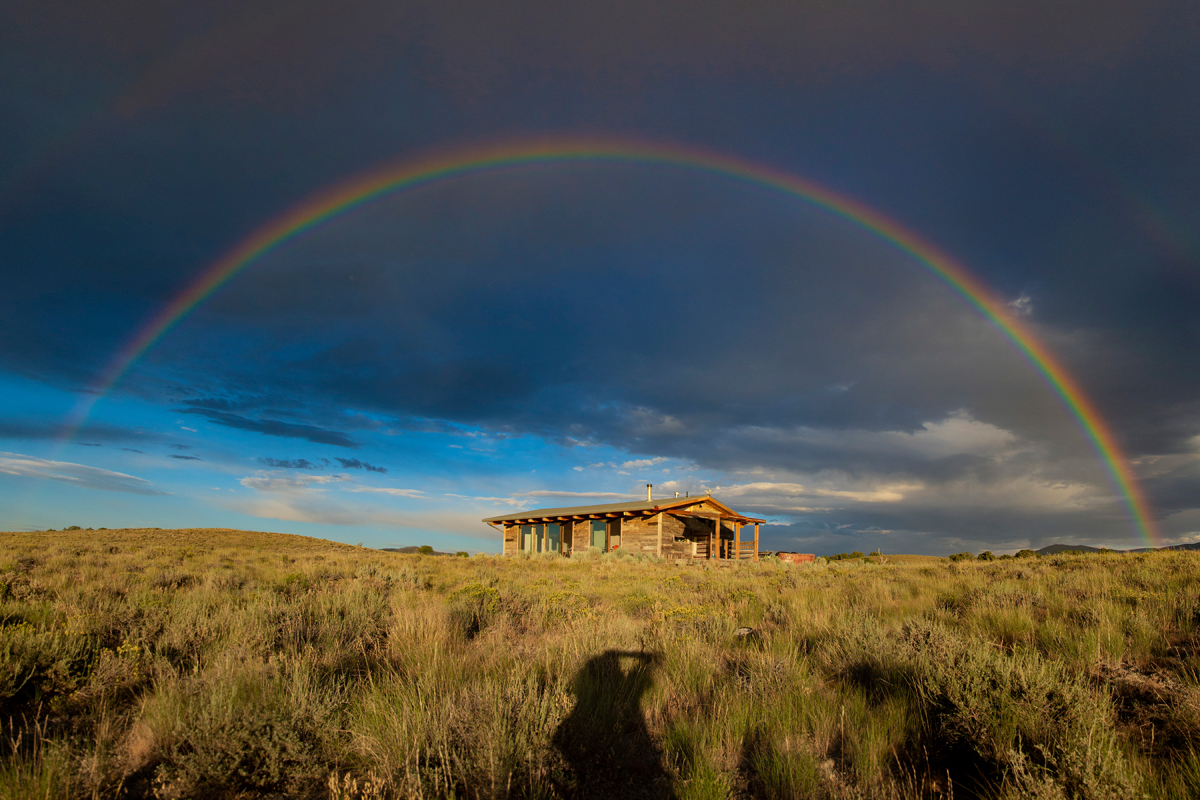 A sunlit cabin beneath a full rainbow in Nevada.