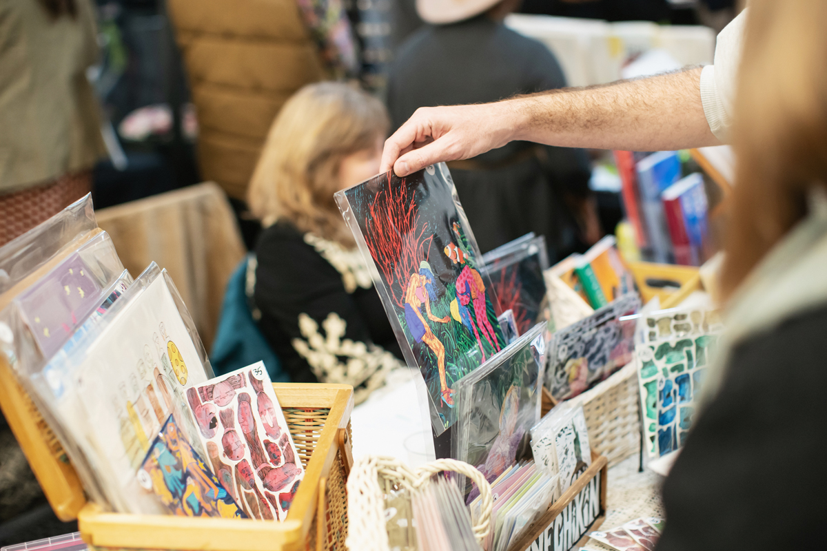 A gallery visitor browses colorful prints at a holiday market.