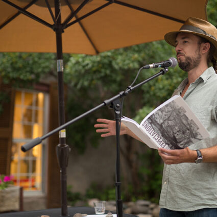 An independent book publisher holds a book aloft and reads into a microphone. Zach Hively of Casa Urraca is part of a fresh wave of New Mexico Indie Book Publishing.