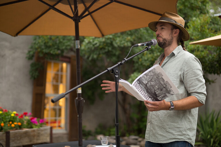 An independent book publisher holds a book aloft and reads into a microphone. Zach Hively of Casa Urraca is part of a fresh wave of New Mexico Indie Book Publishing.