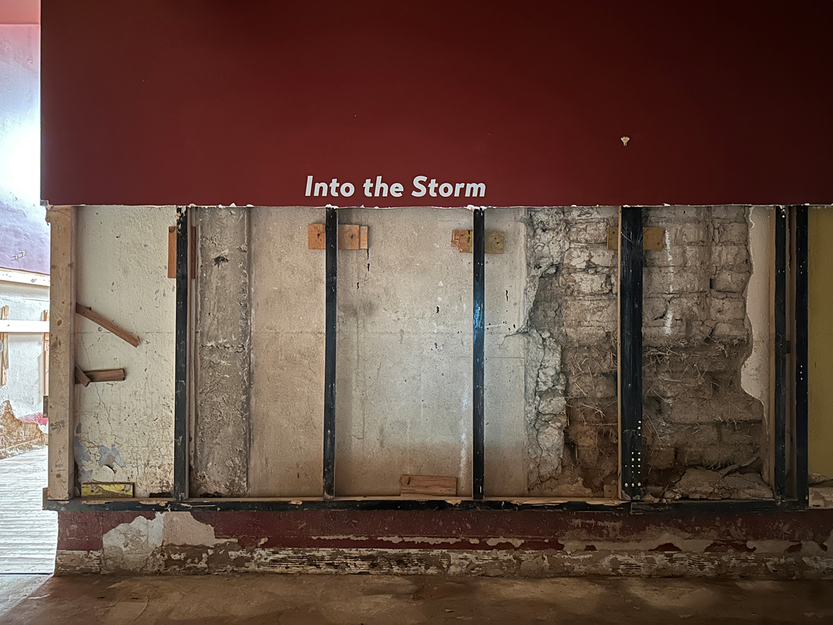 Gutted wall in the Roswell Museum, with surviving vinyl lettering that reads "Into the Storm." View imagery and read stories from the Roswell Museum flood.