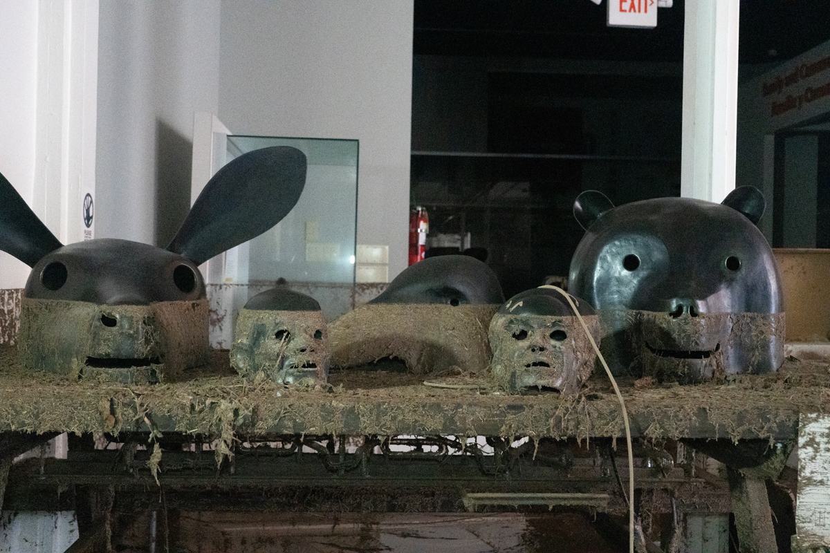 An installation of ceramic animal heads, plastered with mud after a catastrophic flash flood.