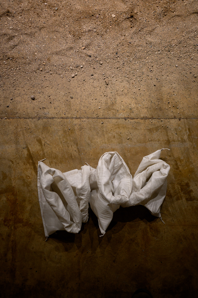 Sacks of soil sit at the edge of a field of scattered earth on a concrete floor, part of Karima Walker's performance series at MOCA Tucson.