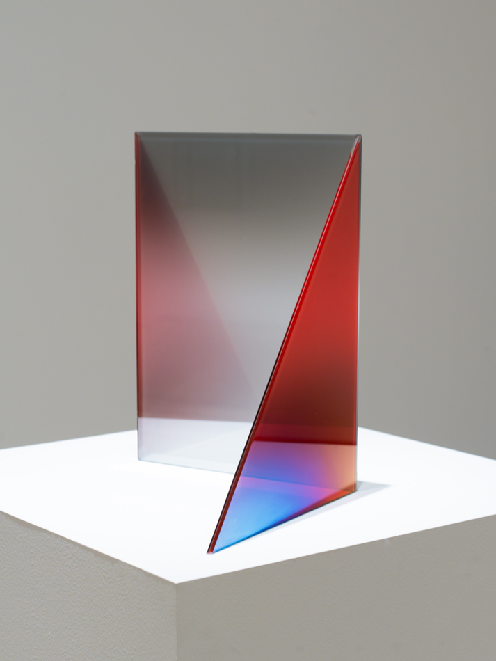 A vertical glass sculptural form by Larry Bell, in vivid gradients of red, blue, purple, and black.