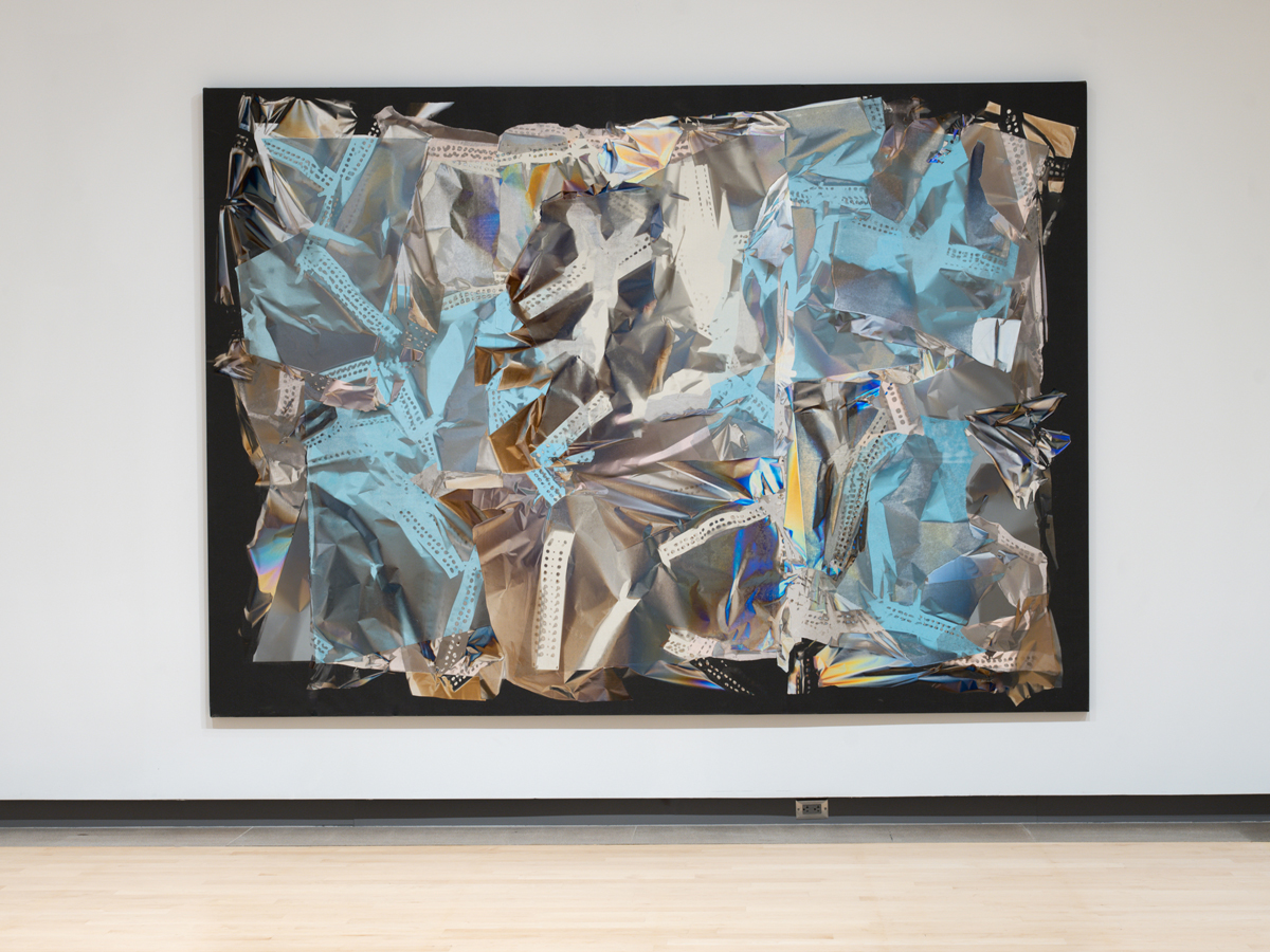 Installation view of a career retrospective by Larry Bell in Phoenix, featuring a wall artwork with crinkled silver-and-blue forms.